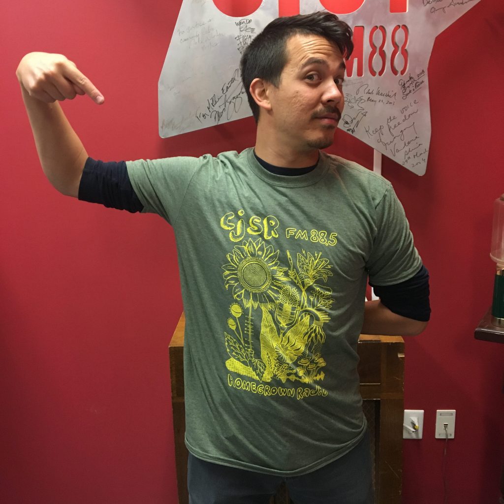 Chris Chang-Yen Phillips shows off a green and yellow t-shirt that says Homegrown Radio