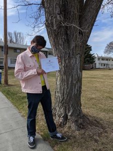 Kaden Peaslee holds up a graduation certificate in front of a tree