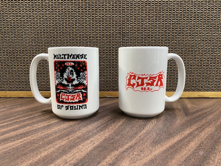 front and back of 2 mugs with FunDrive art, in front of a speaker