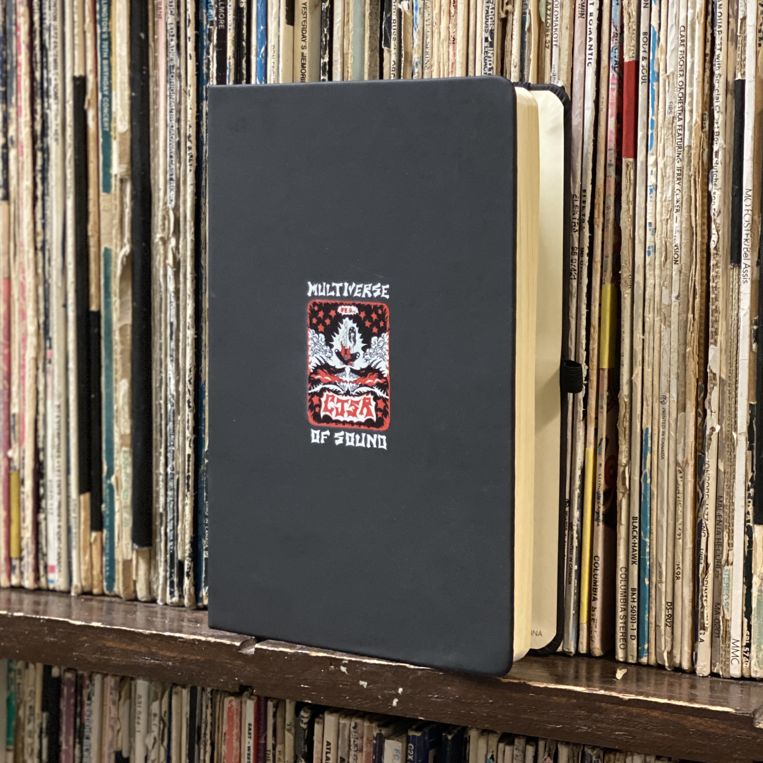 photo of black notebook with CJSR FunDrive artwork on a shelf of well loved vinyl records